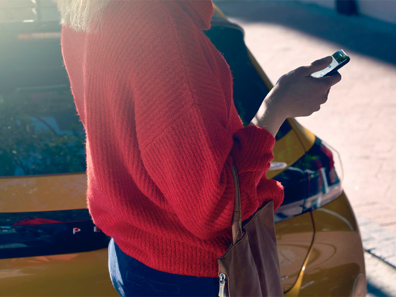 Eine Peugeot Kundin schaut auf Ihre MyPEUGEOT App, die mit Ihrem Auto verbunden ist.
